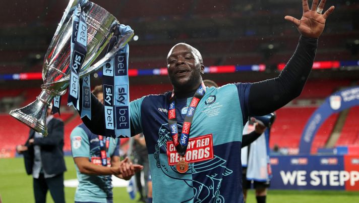 LONDON, ENGLAND - JULY 13: Adedbayo Akinfenwa of Wycombe Wanderers celebrates with the trophy after the Sky Bet League One Play Off Final between Oxford United and Wycombe Wanderers at Wembley Stadium on July 13, 2020 in London, England. Football Stadiums around Europe remain empty due to the Coronavirus Pandemic as Government social distancing laws prohibit fans inside venues resulting in all fixtures being played behind closed doors. (Photo by Catherine Ivill/Getty Images) Wycombe, Akinfenwa si ritira: l’applauso di Wembley per “The Beast” - immagine 1