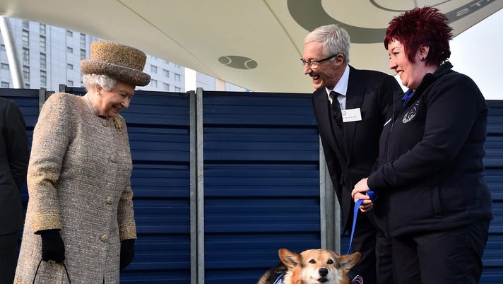 LONDON, ENGLAND - MARCH 17: Britain's Queen Elizabeth II looks at a Corgi dog as British television presenter Paul O'Grady (2nd R) looks on during the opening of the new Mary Tealby dog kennels at Battersea Dogs and Cats Home in London on March 17, 2015. (Photo by Ben Stansall - WPA Pool/Getty Images) Ebouè e i cani della Regina: “Maestà, non voglio più fare il calciatore ma il dog sitter dei suoi corgi!” - immagine 1
