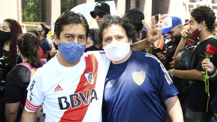 BUENOS AIRES, ARGENTINA - NOVEMBER 26: A River Plate and Boca Juniors fan pose for a picture together as they queue in line to pay tribute to Diego Maradona in the goverment palace on November 26, 2020 in Buenos Aires, Argentina. Maradona died of a heart attack at his home on Thursday 25 aged 60 . He is considered among the best footballers in history and lead his national team to the World Cup in 1986. President of Argentina Alberto Fernandez declared three days of national mourning. (Photo by Rodrigo Valle/Getty Images) Il River regala il titolo al Boca e i tifosi si infuriano: “A quelli non si dà neanche un goccio d’acqua!” - immagine 1